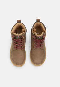 Botas de tobillo marrones de cuero con superficie texturizada, que presentan cordones rojos y grises, un cuello acolchado y una suela de goma natural.