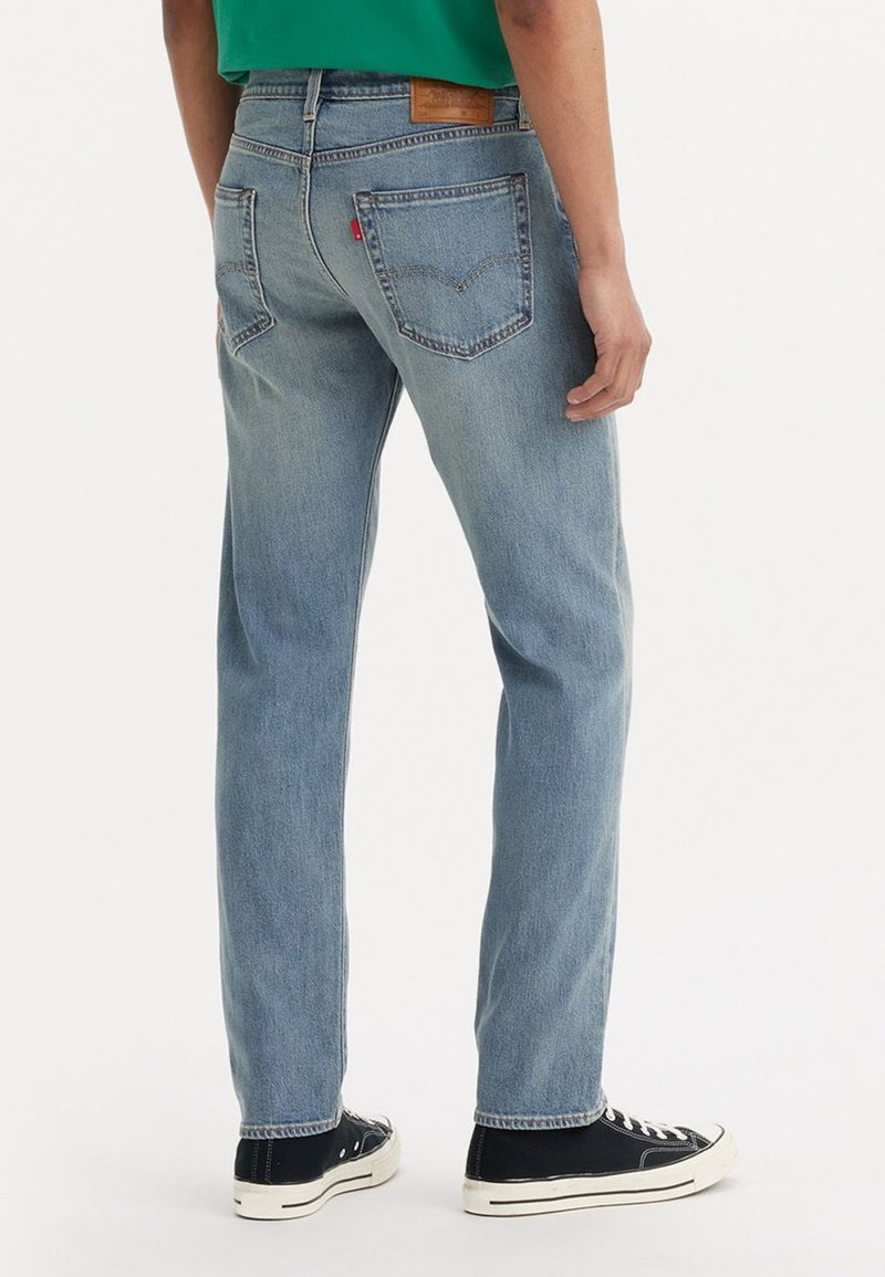 Jeans in denim leggero blu con vestibilità dritta, dotati di tasche posteriori e una targhetta in pelle sulla vita. Abbinati a sneakers nere.