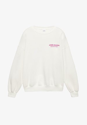 Biely sveter s dlhými rukávmi, rebrovanými manžetami a spodným lemom, s ružovým textom: "APRÈS SEASON Beyond the Slopes" na prednej strane. Mäkká textúra.
