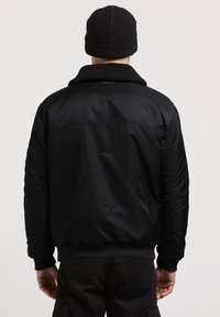 Sort bomberjakke med en tekstureret fleecekrave. Har gatherede ærmer og en ribbet kant. Designet er glat og let.