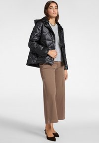 Chaqueta acolchada negra con capucha, botones frontales y bolsillos, llevada sobre un suéter de punto en gris claro y pantalones de pierna ancha color beige.