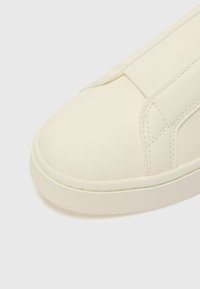 Sneaker bianco slanciato con punta arrotondata, fascia elastica sulla parte superiore, finitura opaca liscia e suola in gomma testurizzata.