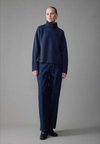 Dark blue knit sweater with a high ribbed collar, paired with relaxed-fit blue denim jeans and black ankle boots. Simple, textured design.