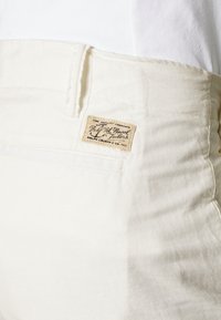 Bílé bavlněné kalhoty s texturovaným povrchem. Mají prošitou pasovku a vintage štítek na zadní kapse.