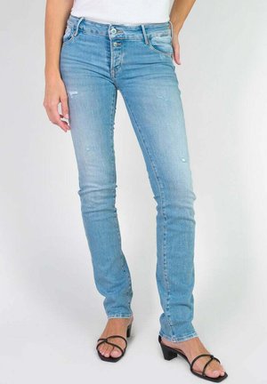 Helle blaue Denim-Jeans mit Slim-Fit, mit leichter Zerrissung und klassischem Fünf-Taschen-Design. Kombiniert mit schwarzen Riemchensandalen.