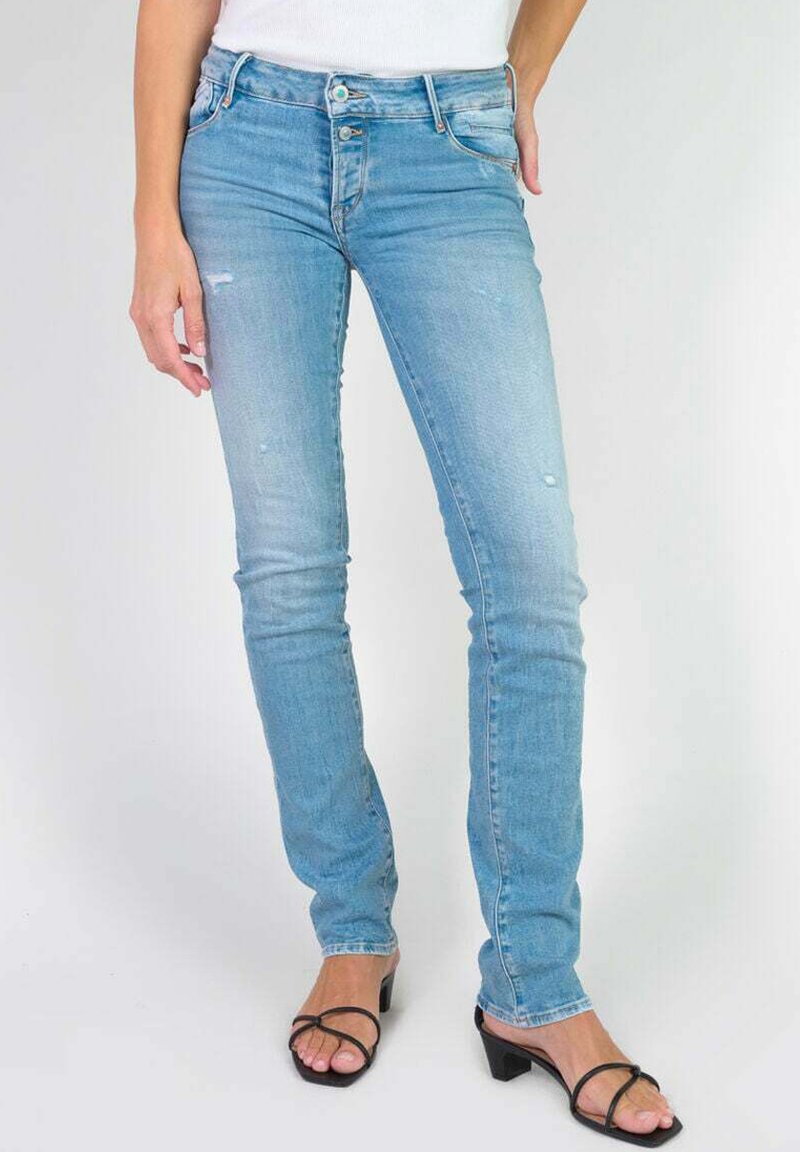 Jean en denim bleu clair avec une coupe slim, présentant de légers effets de décoloration et un design classique à cinq poches. Accompagné de sandales noires à brides.