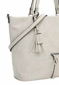 Witte neplederen tote bag met een gestructureerde vorm, slanke schouderband, zilveren hardware en een decoratieve kwast die aan de rits hangt.