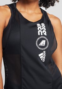 Canottiera sportiva nera con lati in rete, con logo bianco Adidas e stampa grafica. Design elegante con taglio aderente e stile racerback.