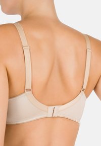 Reggiseno beige con spalline regolabili, tessuto liscio, bordi rifiniti e chiusura a gancio e occhiello sul retro. Design minimal, aspetto senza cuciture.