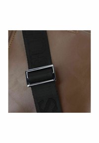 Borsa in pelle marrone con una tracolla intrecciata nera e accessori in argento, che presenta una texture liscia e un delicato motivo a rilievo.