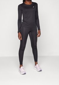 Czarny, długi rękaw sportowy t-shirt i dopasowane legginsy, wykonane z gładkiego materiału. Posiada subtelne logo na piersi i przy kostce. Lekki obuwie sportowe.