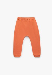 Pomarańczowe spodnie dresowe z elastycznym pasem i elastycznymi mankietami, charakteryzujące się gładką teksturą i luźnym krojem dla komfortu.