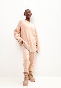 Suéter grande color durazno con ribetes grises, combinado con joggers a juego. El modelo lleva botas de plataforma beige con cordones. Textura suave y ajuste relajado.