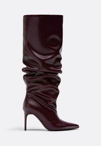 Burgundské nadkolenné čižmy na vysokom podpätku vyrobené z lesklej kože s voľným dizajnom a špicatou špičkou. Obsahuje stiletto podpätok.