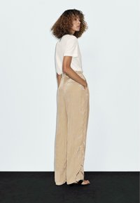 Lange beige broek van textuur stof, met een hoge taille en zijzakken, gecombineerd met een eenvoudig wit t-shirt en sandalen.