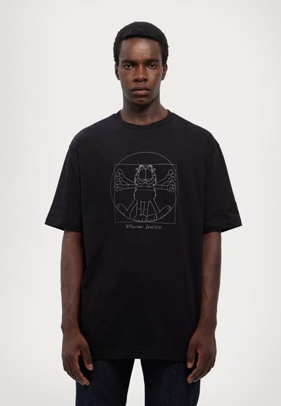 Črna bombažna majica s kratkimi rokavi, ki ima na sredini prsnega dela velik, obrisan risan grafični motiv mačke z razprtimi rokami, z ohlapnim krojem.