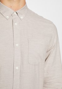 Lichtbeige overhemd met knoopsluiting in een gestructureerde stof, met een klassieke kraag en een enkele borstzak, met witte knopen.
