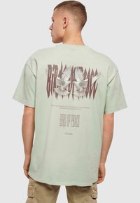 Mint green short-sleeve t-shirt featuring a graphic design of two white doves, text "BIRD OF PEACE" in stylized brown letters.
