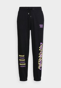 Svarta sweatpants i bomull med elastisk midja och muddar. Tryckt text i lila och gula accenter längs sidorna.