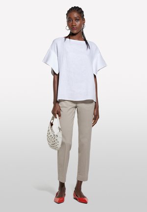 Haut en lin blanc à manches larges, pantalon beige droit, ballerines rouges et un sac blanc avec des clous décoratifs. Design simple et épuré.