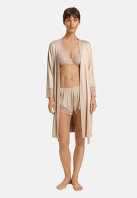 Roba satinate color beige chiaro con dettagli in pizzo, indossata sopra un reggiseno e un paio di pantaloni corti abbinati con bordi in pizzo, caratterizzata da una vestibilità rilassata e una caduta fluida.