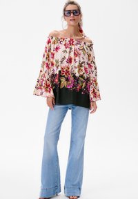 Blumenbluse mit schulterfreiem Design in Pink und Grün mit Glockenärmeln, kombiniert mit hochgeschnittenen hellblauen Schlagjeans.
