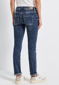 Jeans skinny in denim blu scuro con un lavaggio sbiadito, design a cinque tasche e orli arrotolati, abbinati a scarpe da ginnastica bianche per un contrasto.