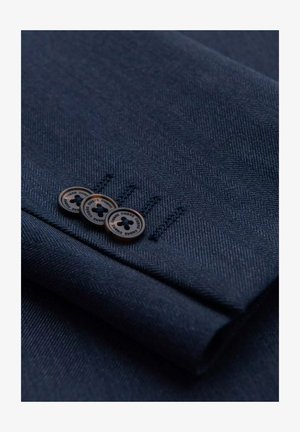 Marineblauw visgraatstof met een gestructureerde afwerking, voorzien van drie bruine knopen en subtiele stikdetails op de manchet.