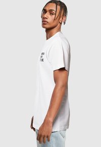 Hvid bomulds t-shirt med korte ærmer, prydet med sort tekst "ALDRIG TIL TID" på fronten, afslappet pasform, glat tekstur.