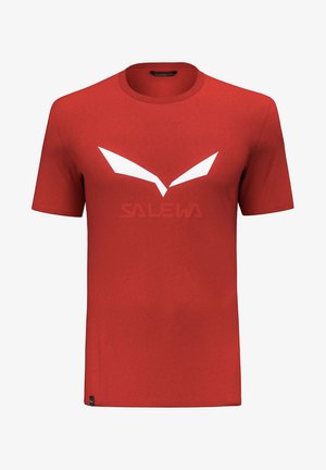 T-shirt rouge à manches courtes avec col rond, présentant un logo angulaire blanc et le nom de la marque "SALEWA" faiblement visible sur la poitrine.