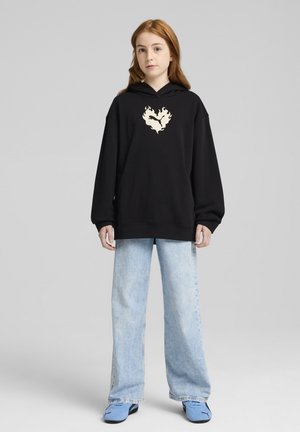 Felpa nera oversize con un design a fiamma crema sul petto, abbinata a jeans dritti blu chiaro e sneakers blu.