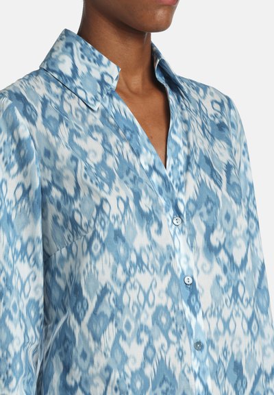 Modrá vzorovaná košeľa s pohodlným strihom, ktorá má klasický golier, zapínanie na gombíky vpredu a mäkkú textúru látky, zobrazujúcu rôzne odtiene modrej.