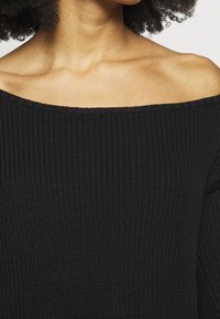 Černý pletený svetr bez ramínek s texturovaným vzorem. Obsahuje žebrované detaily a uvolněný střih kolem výstřihu.