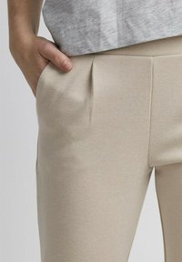 Beige op maat gemaakte broek met een gestructureerde stof, voorzien van zijzakken en subtiele plooien. De tailleband is soepel en zit op de heupen.