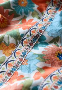 Färggängig blommig tyg med blå, orange och gröna blommor, prydligt dekorerad med en kant längs sömmen och en mjuk, texturerad yta.
