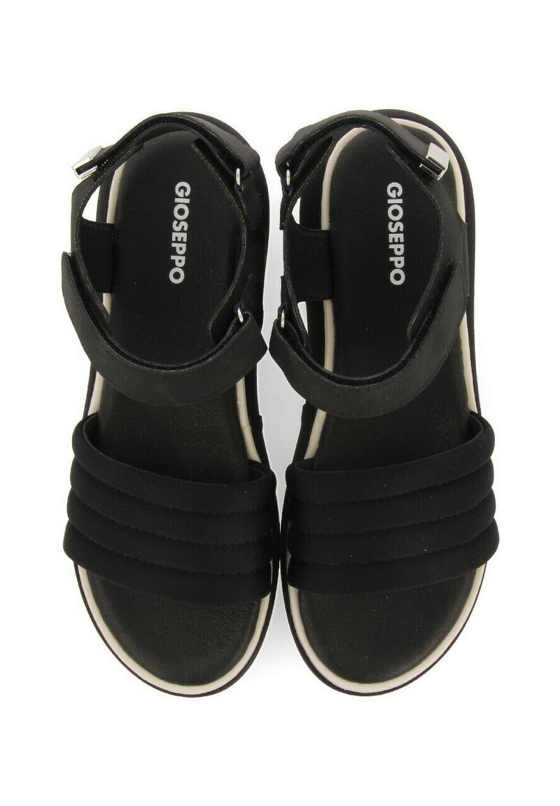 Sandalias negras con un diseño de tiras acolchadas, que presentan correas ajustables en el tobillo y una suela exterior blanca. Nombre de la marca "Gioseppo" visible en el interior.