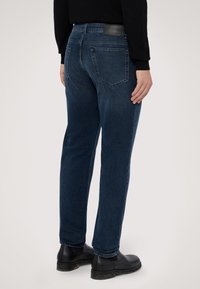 Vaqueros de mezclilla azul oscuro con corte recto, que cuentan con dos bolsillos traseros y un parche de cuero en la cintura. Textura suave y diseño clásico.