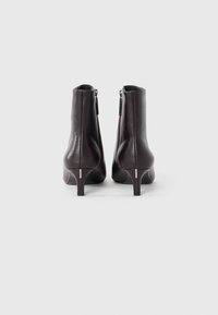 Une paire de bottines en cuir marron foncé avec des zips arrière et de petits talons, présentées de dos sur un fond blanc.
