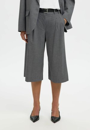 Culottes larges à rayures grises associées à un blazer assorti, ceinture noire, chemise blanche et escarpins noirs à bouts pointus.