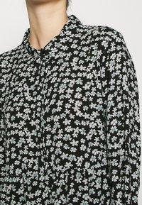 Abito nero a fiori con colletto, caratterizzato da un motivo di fiori bianchi e verde chiaro. Tessuto fluido con un design plissettato.