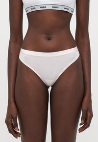 String en mélange de coton rose clair avec une ceinture élastique douce arborant un logo en relief. Texture lisse, design minimaliste et coupe taille basse.