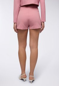 Pantaloni corti rosa su misura con una texture liscia, caratterizzati da una vita alta e un orlo pulito. Abbinati a tacchi aperti di colore chiaro.