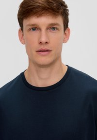 Tumed sinine ümar kaelusega t-särk, mis on valmistatud pehmest kangast, regulaarse lõike ja minimalistliku disainiga, ilma nähtavate mustrite või graafikata.
