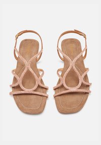 Sandalias de tiras en color oro rosa con textura de ante sintético, que presentan un ribete de joyas y un diseño circular en las tiras superiores.