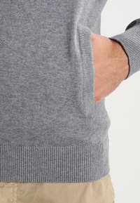 Gray knitted sweater with ribbed hem and cuffs, featuring a side pocket and soft texture. Fabric appears smooth and lightweight.