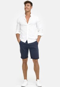 White linen shirt with button-down collar, navy shorts with rolled cuffs, and white sneakers. Simple and casual summer outfit.