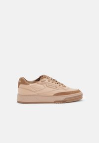 Beige leather sneakers with contrasting suede accents, flat laces, padded tongue, and a textured rubber sole featuring grooves.