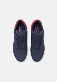Ténis desportivos azul-marinho com detalhes vermelhos, design com atacadores, material sintético suave e secções perfuradas para respirabilidade.