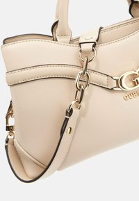Beige neplederen handtas met gouden hardware, dubbele handgrepen en een afneembare schouderband. Voorzien van contrasterende stiksels en logo-detail.