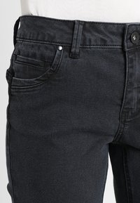 Black denim jeans featuring a slim fit, five-pocket design, and a button closure. The fabric has a smooth texture and slight stretch.